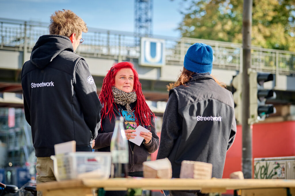 Zwei Streetworker stehen einer Frau mit roten Dreadlocks gegenüber